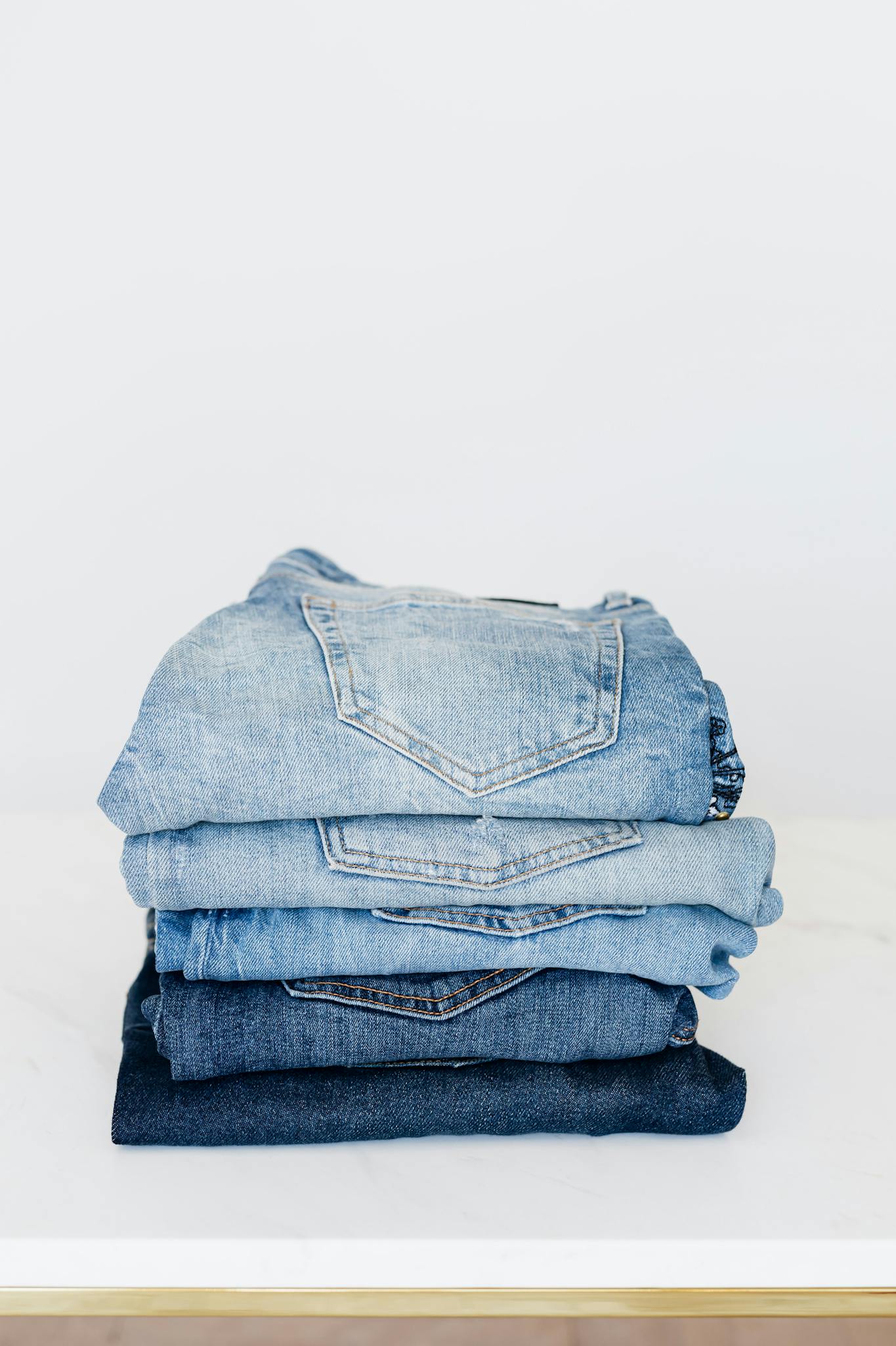 Pile of denim pants of different shades of blue placed on white shelf